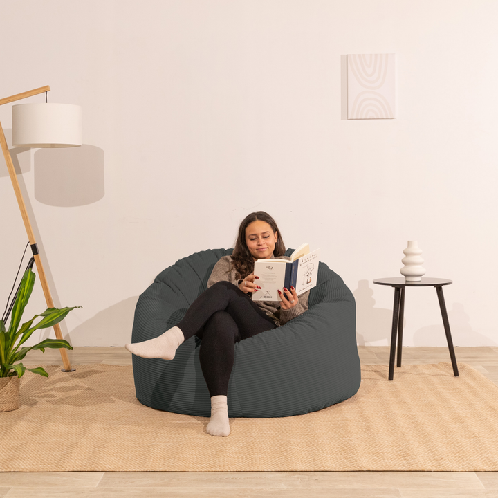 Pouf en velours côtelé épais gris foncé, personne assise pour lire