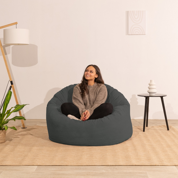 Pouf en velours côtelé épais gris foncé, personne assise au centre