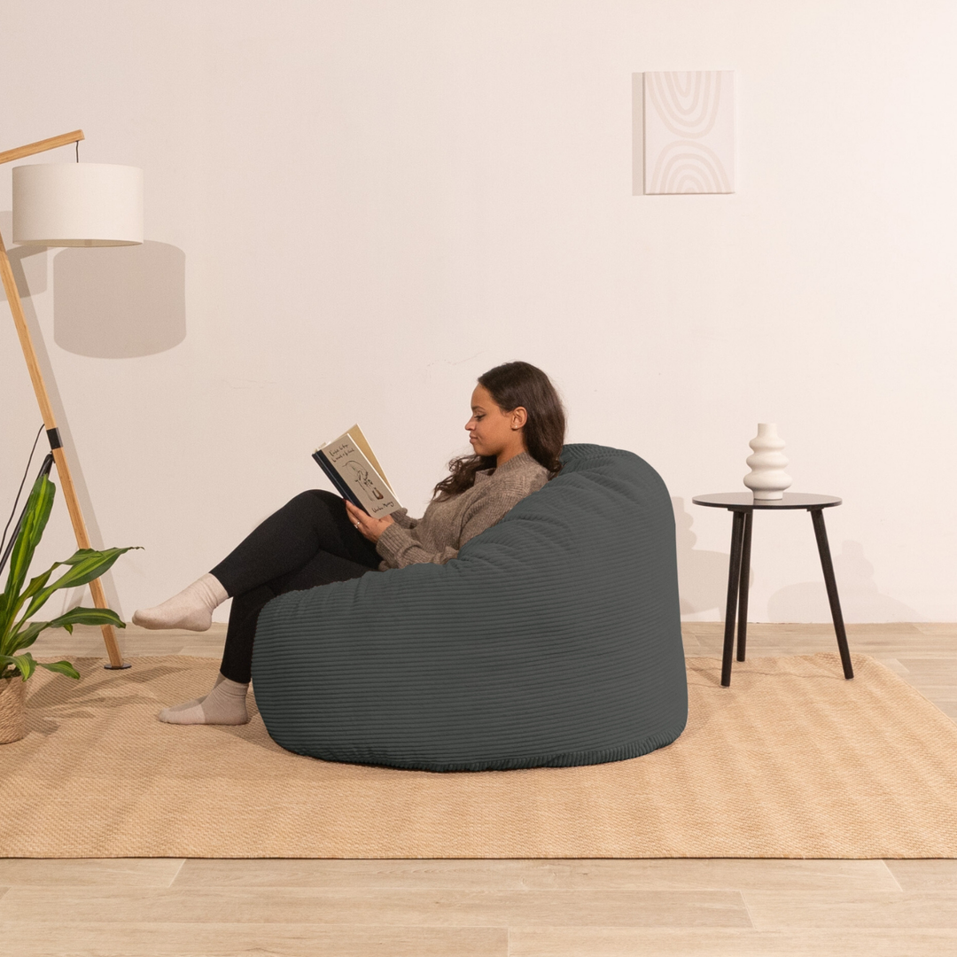 Pouf en velours côtelé épais gris foncé, personne assise lisant